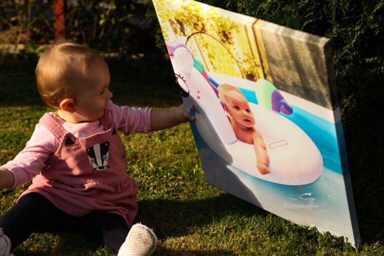 Beba sjedi na travi i drzi svoju fotografiju na platnu