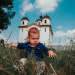 Fotografija bebe koja sjedi u travi ispred crkve